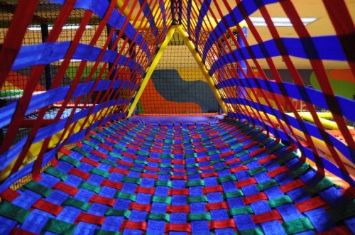 Colorful netting and padded flooring create a vibrant play area in a children's indoor playground.