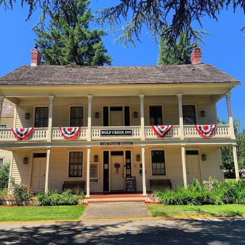 Historic building with a porch, decorated with red, white, and blue bunting, surrounded by trees. Sign reads "Wolf Creek Inn."