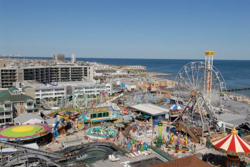 A vibrant amusement park by the ocean, featuring rides, games, and colorful attractions under a clear blue sky.