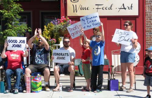 A group of people holding signs in support of someone named John, celebrating with smiles and cheers outside a venue.