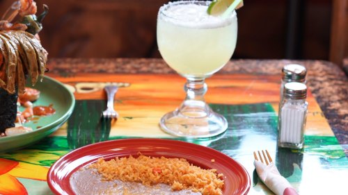 A plate of rice on a colorful table, with a margarita and condiments in the background.