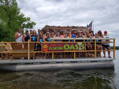 A large group of people poses on a floating platform with a sign that reads "Billy Lake Floating Oasis."