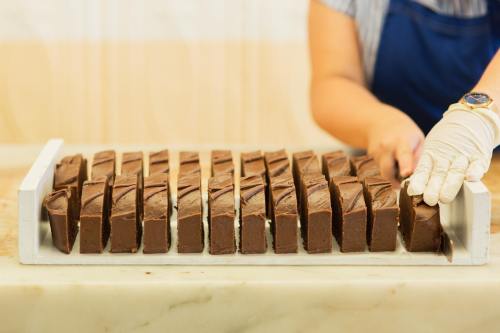 A person in gloves cuts chocolate fudge into squares on a marble surface.