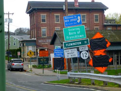 Road signs indicating entry into Frenchtown, New Jersey, with construction signs and a historic building in the background.