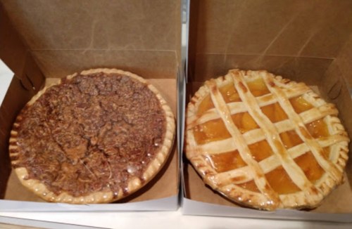 Two pies in cardboard boxes: one pecan pie and one peach pie with a lattice crust.
