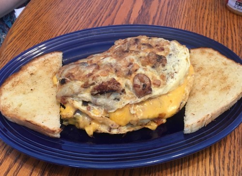 A large cheese omelet with mushrooms and toast on a blue plate, served on a wooden table.