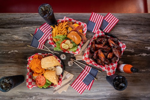 A table with baskets of burgers, wings, fries, and drinks, decorated with small American flags.