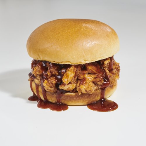 A close-up of a sandwich with shredded chicken and barbecue sauce on a soft bun, set against a plain background.