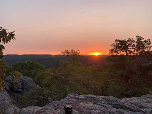 A scenic view of a sunset over a mountainous landscape, with trees and rocky terrain in the foreground.