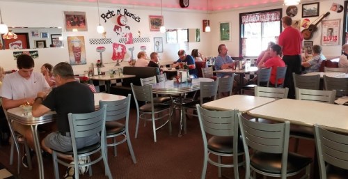 A busy diner with patrons at tables, enjoying meals in a retro-style setting with vintage decor.