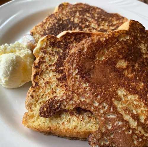 Three slices of golden-brown French toast served with a dollop of butter on a white plate.