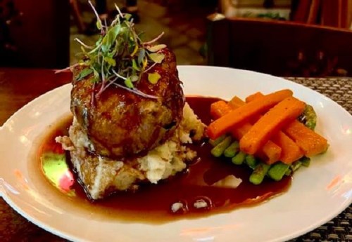 A plated meal featuring a meatloaf topped with greens, mashed potatoes, and a side of glazed carrots and asparagus.