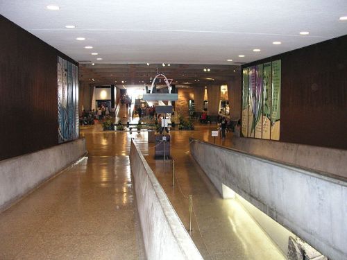 Interior view of a spacious, modern hallway with artwork on the walls and a smooth, wide walkway leading to a busy area.