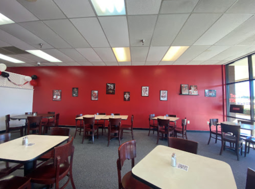 Interior of a restaurant featuring red walls, tables with chairs, and framed pictures on the wall.