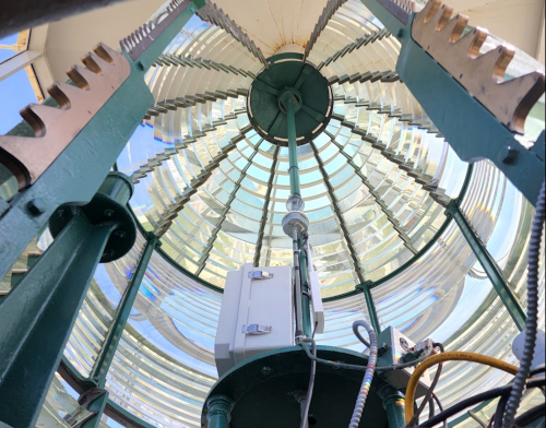 View from inside a lighthouse, showcasing the intricate glass lens and metal structure above.