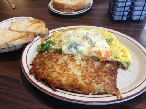 A plate with a vegetable omelet topped with cheese, crispy hash browns, and two slices of toasted bread on the side.