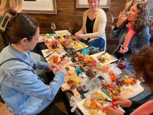 A group of friends enjoying a charcuterie board and wine, laughing and sharing food at a cozy gathering.