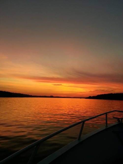 A serene sunset over a calm lake, with vibrant orange and pink hues reflecting on the water.