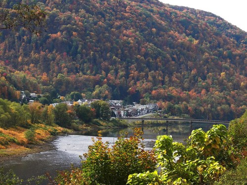 A scenic view of a river surrounded by colorful autumn foliage and a small town nestled in the valley.