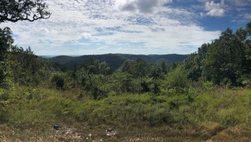 A panoramic view of rolling hills and lush greenery under a partly cloudy sky.