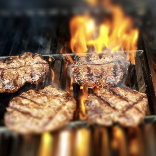 Grilled steaks sizzling on a barbecue with flames and smoke rising.