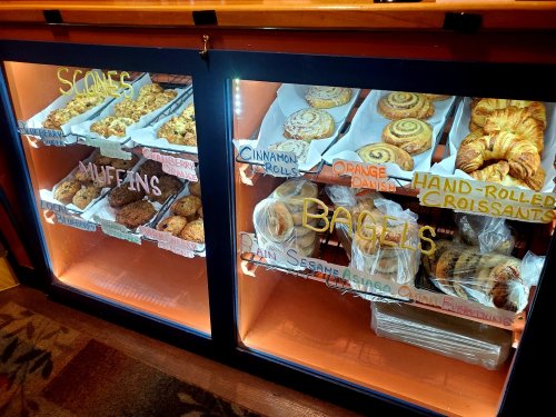 Display case filled with various baked goods, including scones, muffins, bagels, cinnamon rolls, and croissants.