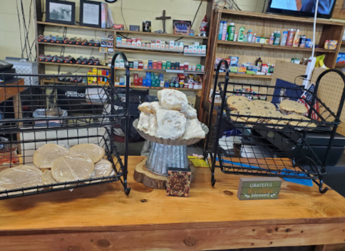 Two wire racks display cookies, with a stack of cookies on a wooden stand in a cozy shop setting.