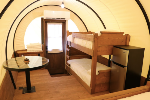 Cozy interior of a glamping tent featuring bunk beds, a small table, and a mini fridge.