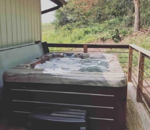 A hot tub on a wooden deck surrounded by greenery and trees in a peaceful outdoor setting.