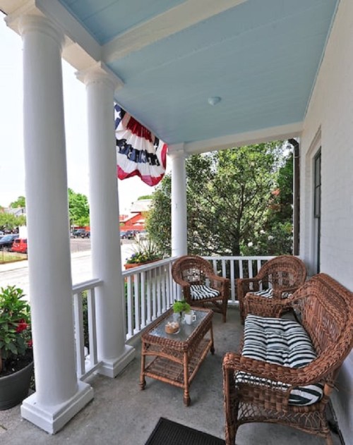 A cozy porch with wicker furniture, a small table, and a blue ceiling, decorated with patriotic bunting.