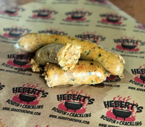 Three pieces of boudin sausage on branded paper, showcasing a golden-brown exterior and visible rice filling.