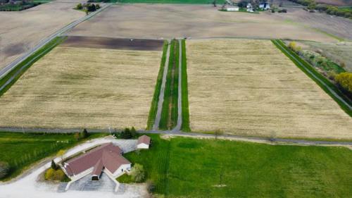 Aerial view of a rural landscape with fields, a road, and a small building at the edge of the property.