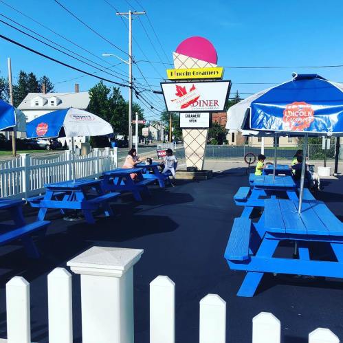 Outdoor seating area with blue picnic tables at a diner, featuring a large ice cream sign and clear blue sky.