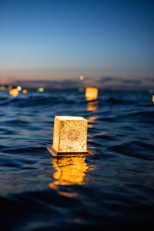 A glowing lantern floats on water at dusk, reflecting light as the sky transitions to night.
