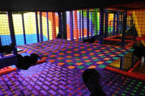 Colorful indoor play structure with a woven mat and netting, surrounded by vibrant walls and play equipment.
