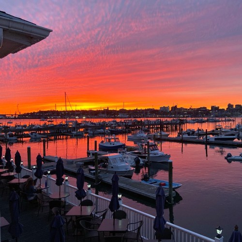 A vibrant sunset over a marina, with boats docked and colorful clouds reflecting on the water.