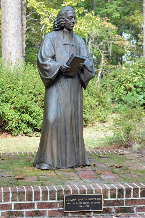 Bronze statue of Johann Martin Bolzius holding a book, set on a brick pedestal in a green park.