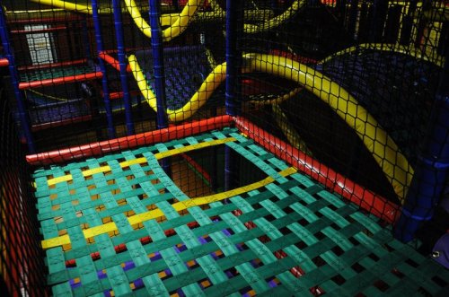 Colorful indoor play structure with a woven floor and tunnels, featuring bright yellow and red elements.