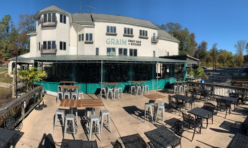 A panoramic view of Grain Craft Bar & Kitchen, featuring outdoor seating and a modern building against a clear blue sky.