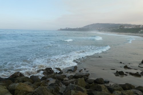A serene beach scene with gentle waves lapping at rocky shores and a misty coastline in the background.