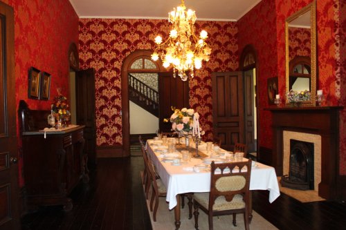 Elegant dining room with a chandelier, floral wallpaper, a long table set for dinner, and a staircase in the background.