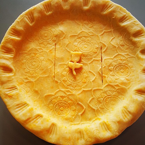 A decorative pie crust with intricate floral patterns and a small figure in the center, ready for baking.
