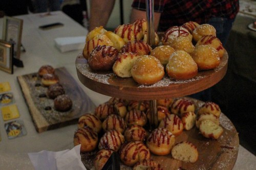 A tiered wooden stand filled with assorted sweet pastries, some drizzled with sauce and dusted with powdered sugar.