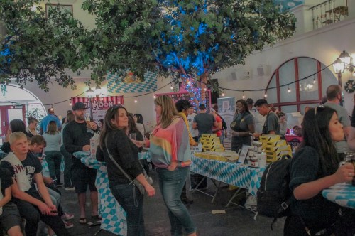 A lively indoor event with people socializing around tables decorated with blue and white checkered patterns.