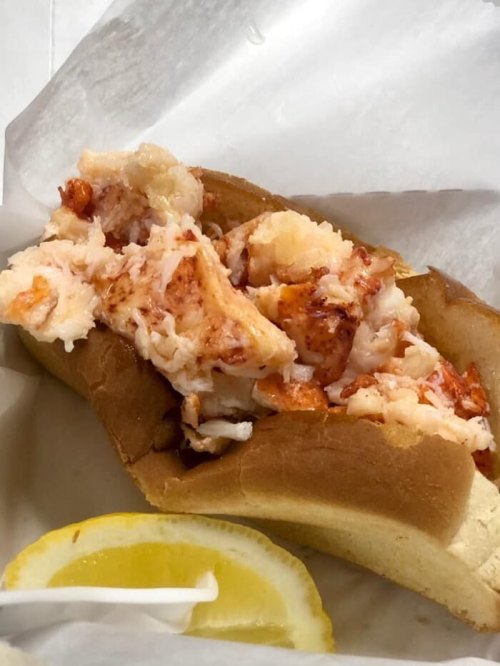 A close-up of a lobster roll filled with chunks of lobster meat, served in a soft bun with a lemon wedge.
