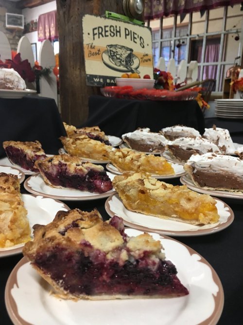 A display of various pie slices on plates, including fruit and cream pies, in a cozy setting with autumn decor.