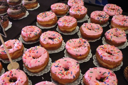 A display of pink frosted donuts with colorful sprinkles on lace doilies.