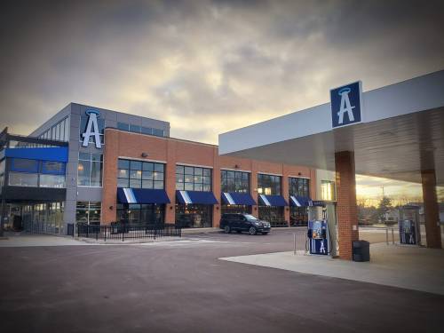 Modern building with large windows and blue accents, featuring a sign with the letter "A" and a parking area.
