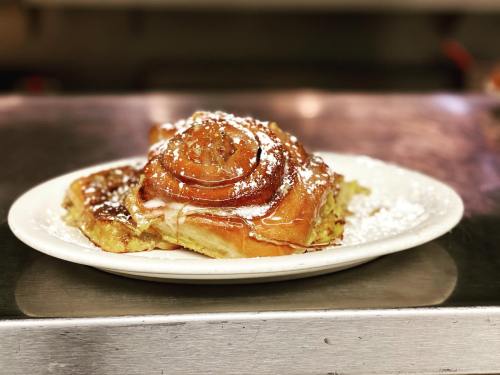 A plate of freshly baked cinnamon rolls drizzled with icing and dusted with powdered sugar.