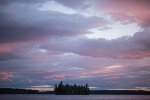 A serene lake at sunset, featuring an island surrounded by calm waters and colorful, cloud-filled skies.